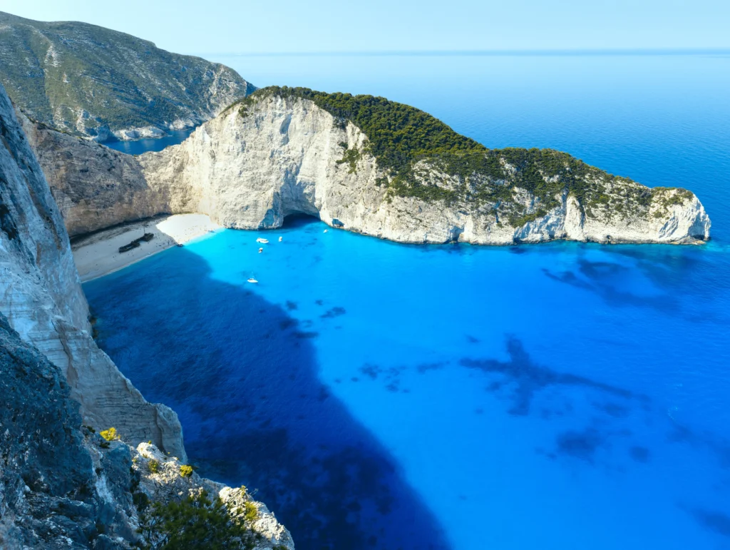 Playa Navagio en Grecia rodeada de imponentes acantilados y aguas cristalinas con un barco naufragado en la arena.