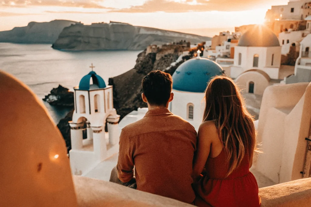 Pareja contemplando una puesta de sol desde una terraza en Santorini, con vistas a las casas blancas y cúpulas azules. Destinos Románticos Viajes Pareja