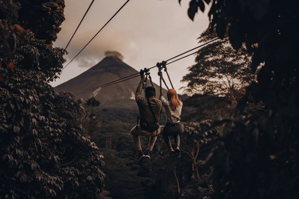 Pareja practicando tirolina en la selva tropical de Costa Rica con un volcán activo de fondo. Destinos Románticos Viajes Pareja