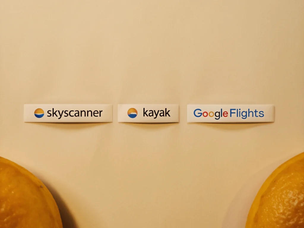 Logotipos de Skyscanner, Kayak y Google Flights en una pantalla, representando herramientas para encontrar vuelos low cost.