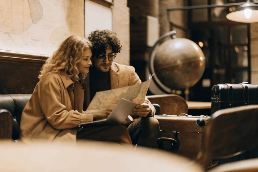 Pareja planificando su próximo viaje romántico con un mapa y una computadora portátil en una acogedora cafetería.