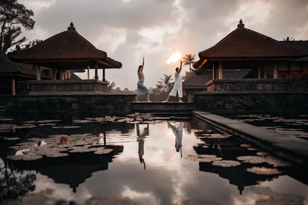 Pareja practicando yoga al amanecer en una plataforma sobre el agua en Bali, rodeados de vegetación tropical y templos balineses.Destinos Románticos Viajes Pareja