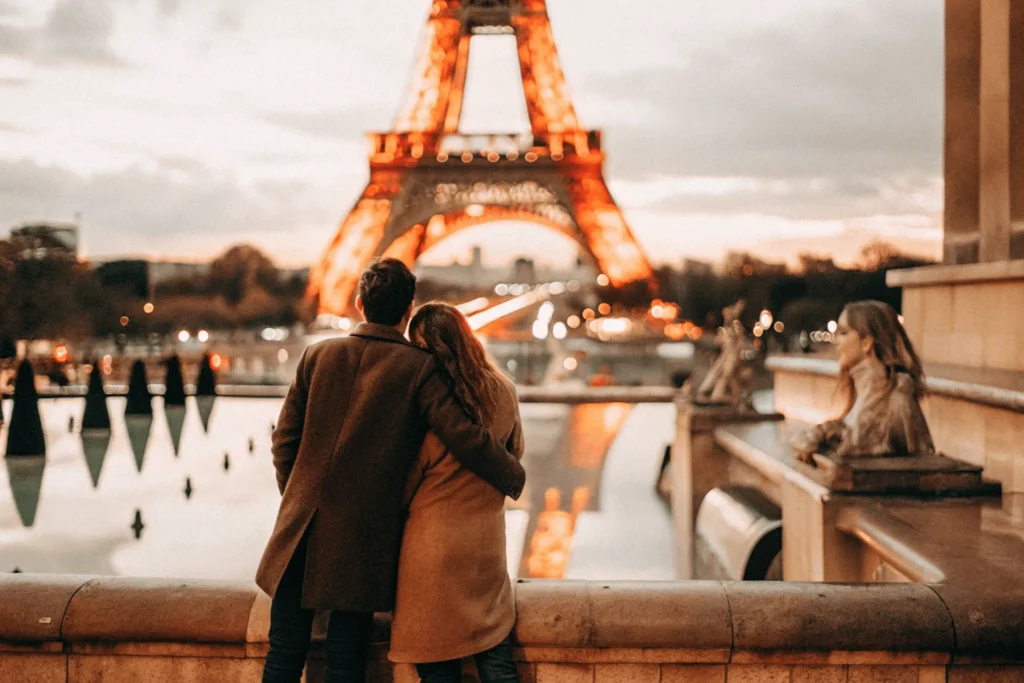 Pareja abrazada frente a la Torre Eiffel iluminada al anochecer.